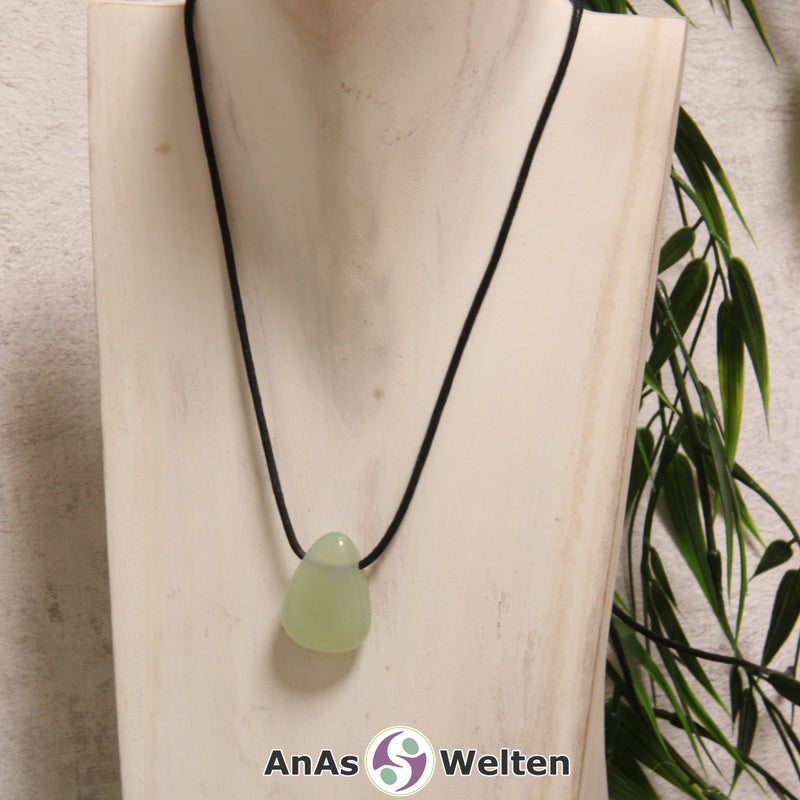 Ein grüner Serpentin gebohrter Trommelstein an einem schwarzen Baumwollband, der um eine helle Büste gehängt wurde.