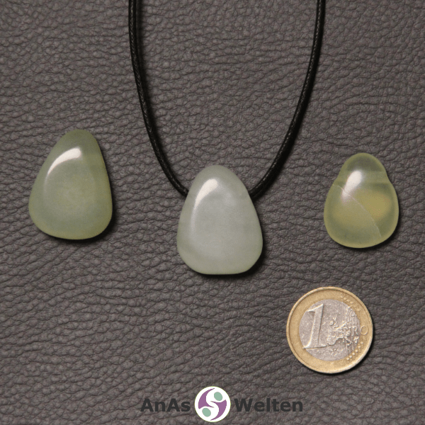 Drei grüne Serpentin gebohrte Trommelsteine nebeneinander. Einer befindet sich an einem schwarzen gewachsten Baumwollband.