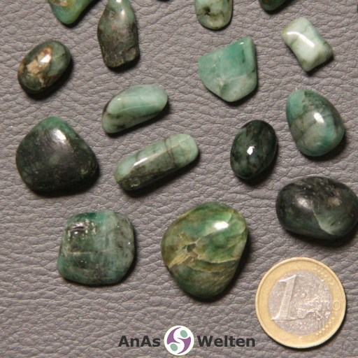 Das Bild zeigt einen Smaragd (grüner Beryll) Trommelstein anhand mehrerer Beispielsteine. Die Edelsteine haben unterschiedliche Grüntöne. Einige sind hellgrün bis fast türkis, während andere ein saftiges und wieder andere ein tiefdunkles Grünhaben, auch schwarzem braune und graue Einschlüsse sind keine Seltenheit.