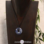 Das Bild zeigt einen Sodalith Donut an einem Baumwollband. Der Edelstein hat eine blau-weiße Musterung. Die beiden Farben sind dabei recht gleichmäßig verteilt.