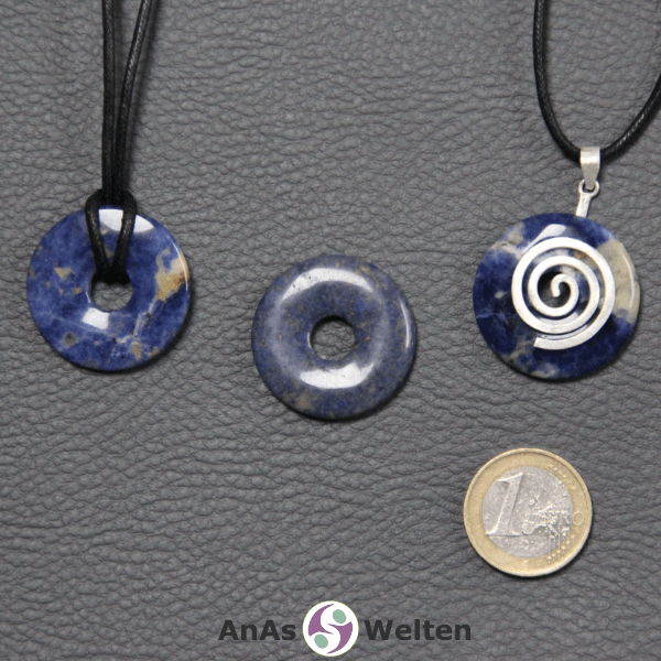 Drei Sodalith Donuts nebeneinander. Einer an einem Baumwollband, ein anderer an einem Donut-Halter mit Baumwollband.