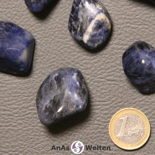 Das Bild zeigt einen Sodalith Trommelstein anhand mehrerer Beispielsteine. Die Edelsteine haben eine dunkelblaue Grundfarbe. Außerdem haben sie schwarze Einschlüsse, weiße Einschlüsse oder beides.