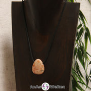 Ein gebohrter Sonnenstein Trommelstein an einem Baumwollband. Der Edelstein hat eine orange-beige Farbe, deren Muster ein wenig an Flammen erinnert.