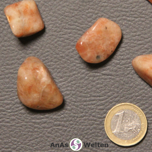 Das Bild zeigt einen Sonnenstein Trommelstein anhand mehrerer Beispielsteine. Die Edelsteine haben eine orange-beige Farbe, deren Musterung an Feuer erinnert. Einige Steine haben gelegentliche Einschlüsse.