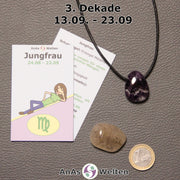 Die Sternzeichenkarte und je ein beispielhafter gebohrter Amethyst Trommelstein am Band und ein Rutilquarz Trommelstein der 3. Dekade liegen nebeneinander.