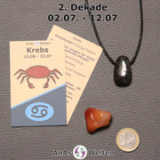 Die Sternzeichenkarte und je ein beispielhafter gebohrter Labradorit Trommelstein am Band und ein Karneol Trommelstein der 2. Dekade liegen nebeneinander.