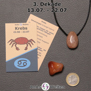 Die Sternzeichenkarte und je ein beispielhafter gebohrter Mondstein Trommelstein am Band und ein Karneol Trommelstein der 3. Dekade liegen nebeneinander.