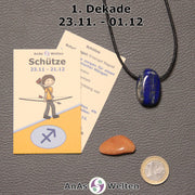 Die Sternzeichenkarte und je ein beispielhafter gebohrter Lapislazuli Trommelstein am Band und ein Dolomit Trommelstein der 1. Dekade liegen nebeneinander.