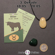 Die Sternzeichenkarte und je ein beispielhafter gebohrter Orangencalcit Trommelstein am Band und ein Malachit Trommelstein der 3. Dekade liegen nebeneinander.