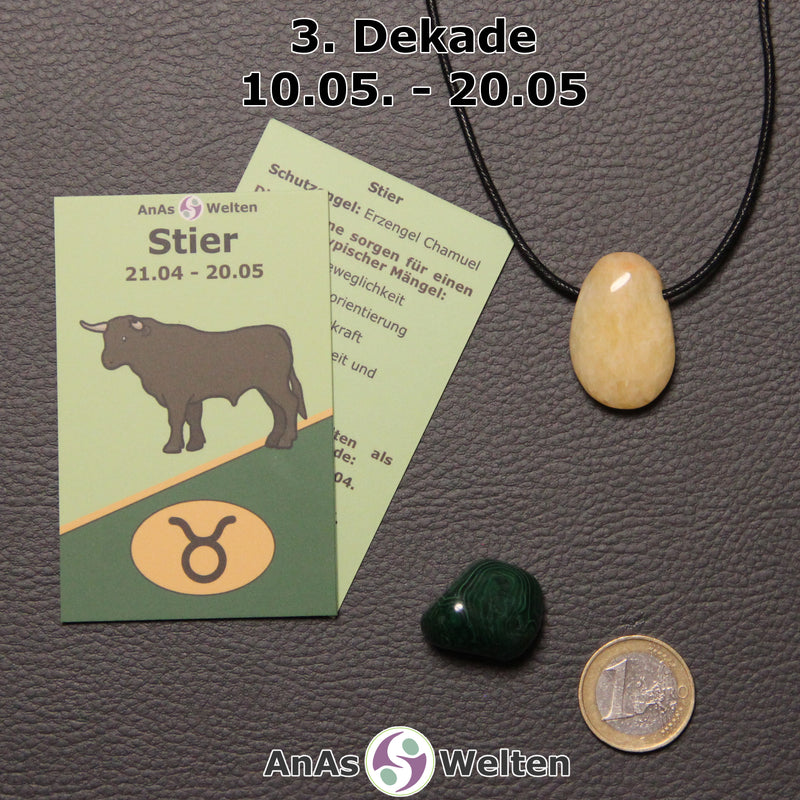 Die Sternzeichenkarte und je ein beispielhafter gebohrter Orangencalcit Trommelstein am Band und ein Malachit Trommelstein der 3. Dekade liegen nebeneinander.
