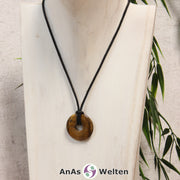 Ein Tigerauge Donut als Kette an einem schwarzen gewachsten Baumwollband um eine weiße Büste.