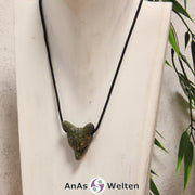 Das Bild zeigt einen Unakit Wolf Anhänger an einem Baumwollband. Der Edelstein unregelmäßig grün und rotbraun gemustert. Das Fellmuster und die Nase sind durch kleine Kerben im Edelstein dargestellt. Die Augen sind kleine schwarze Perlen.