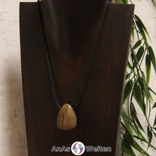 Ein versteinertes Holz gebohrter Trommelstein an einem Baumwollband. Der Edelstein besteht aus verschiedenen Brauntönen, die ähnlich einer Holzmaserung abgeordnet sind.